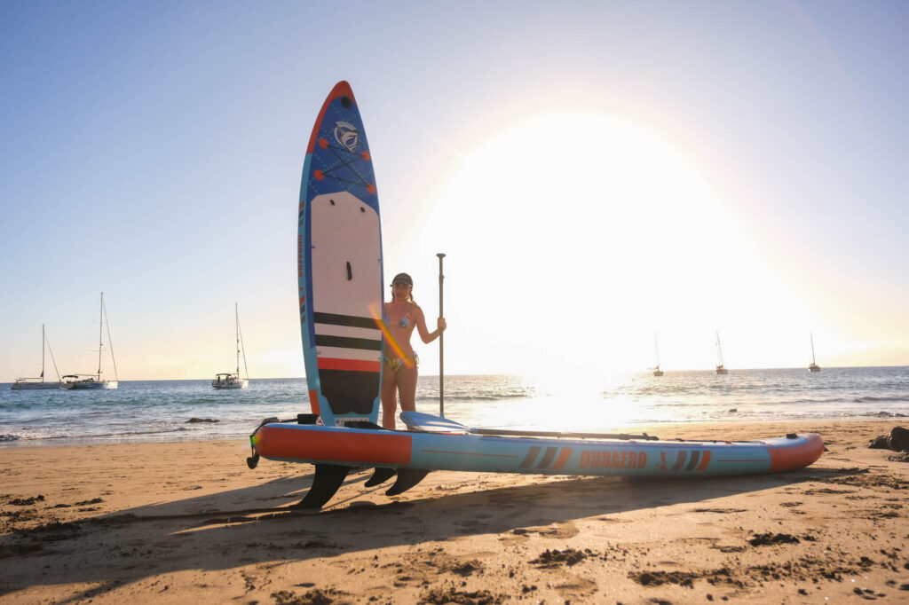 Woman standing with paddleboard and paddle on sandy Tenerife beach at sunset