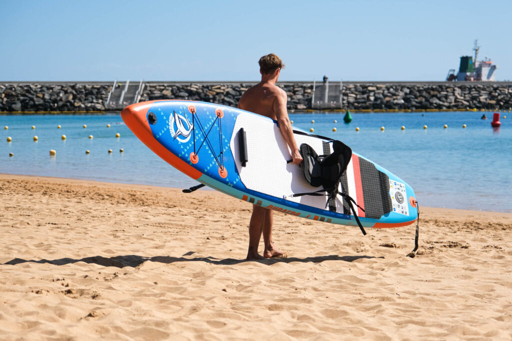 Man holding paddleboard from tralei rentals in Las teresitas, tenerife